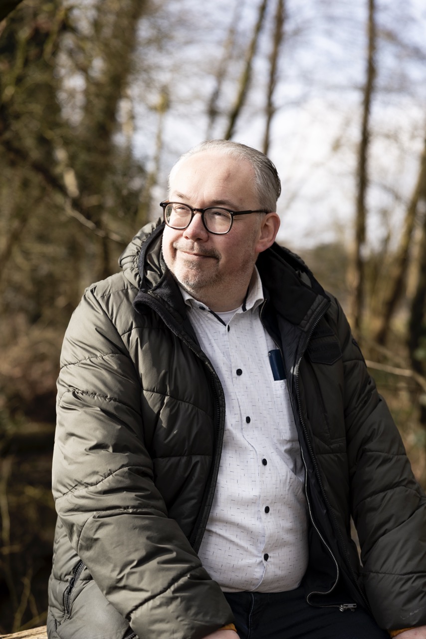 Een man bevindt zich in een bos en kijkt weg van de camera.