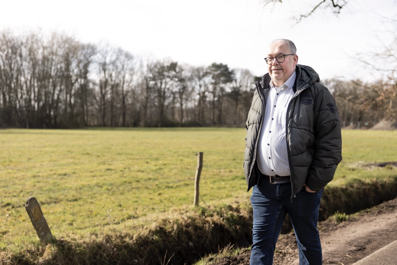 Een man loopt over een weg naast een weiland.